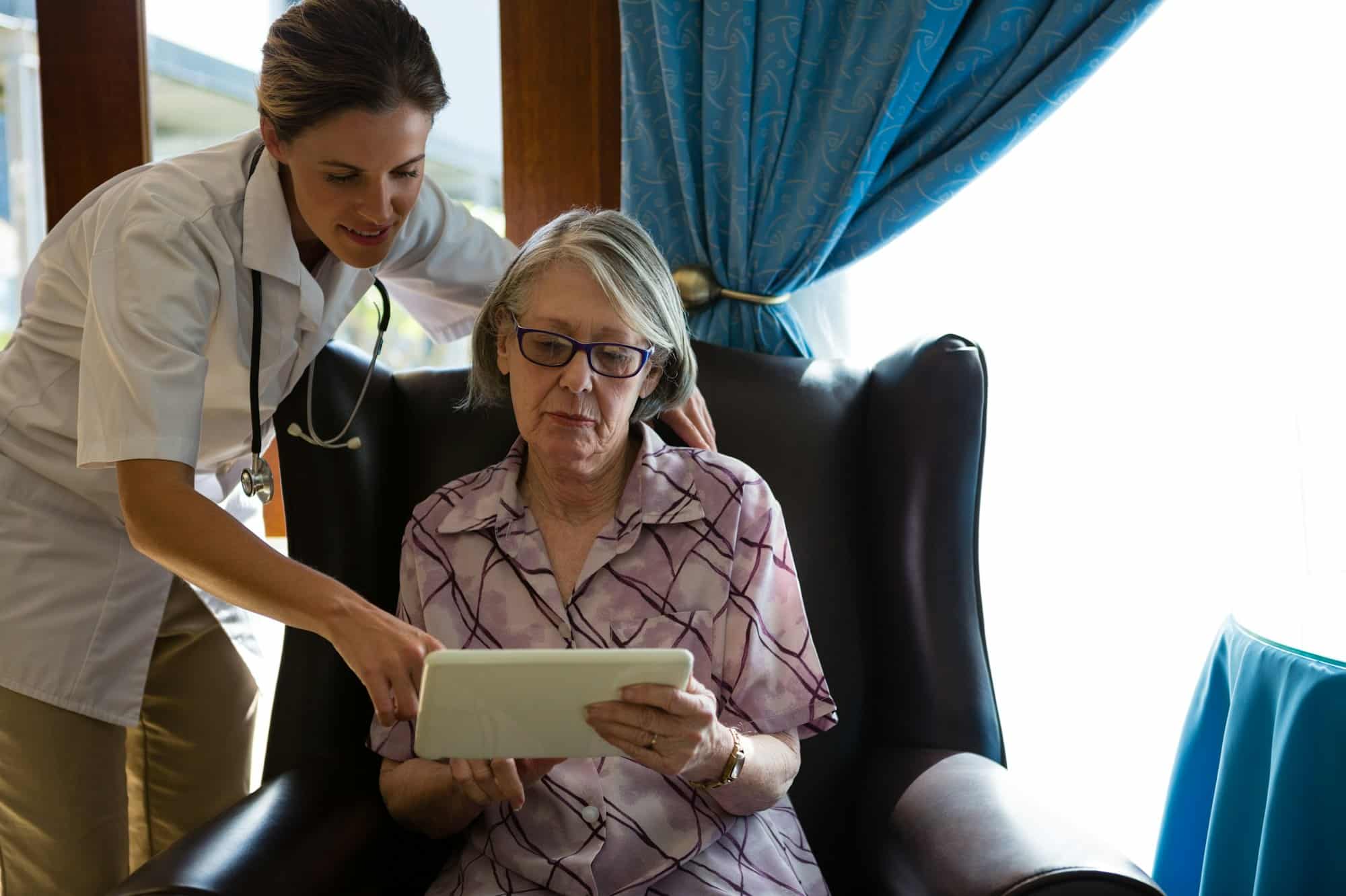 Female doctor assisting woman in using tablet at retirement home