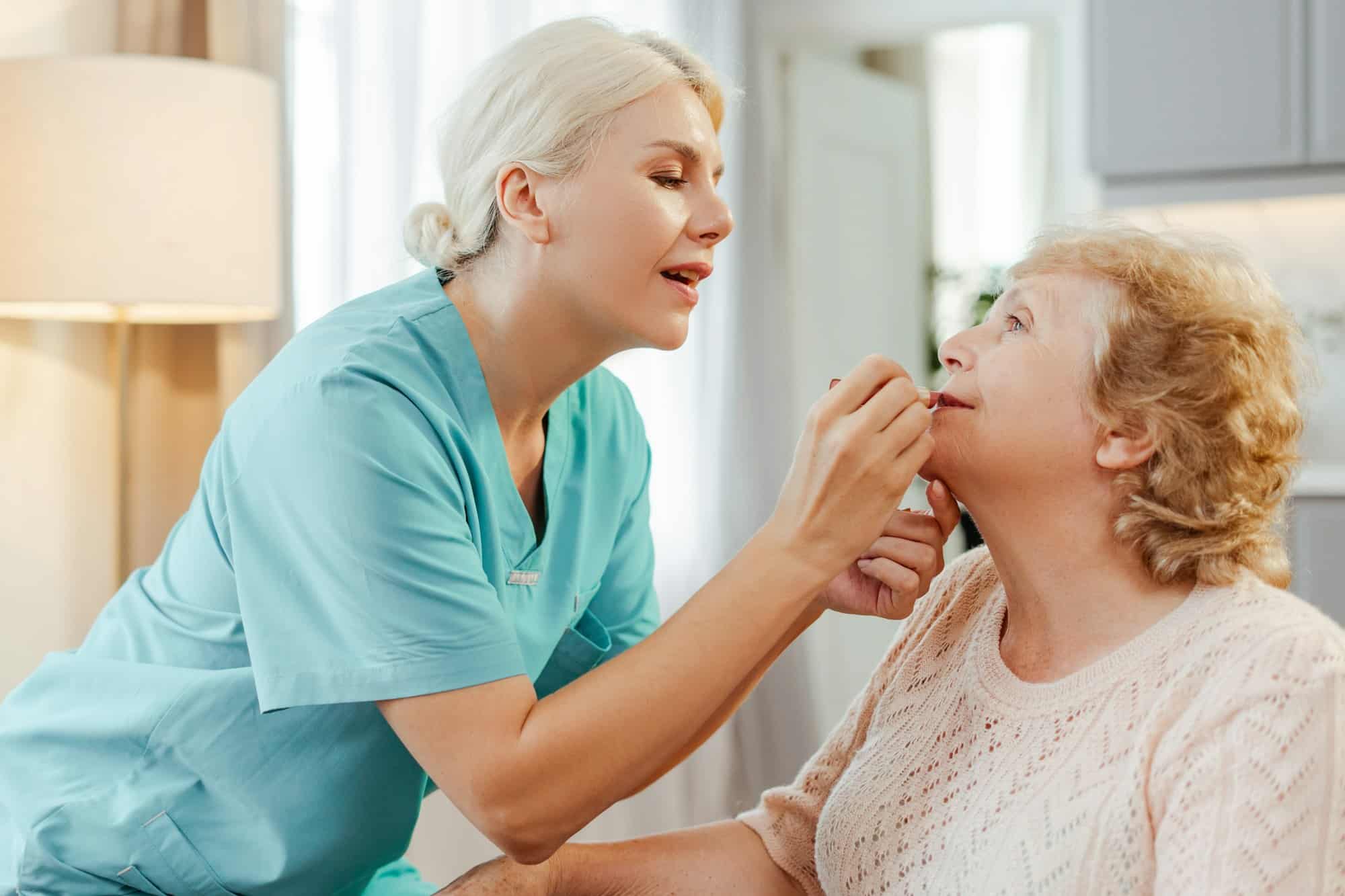 Nurse applying lipstick to senior woman in retirement home